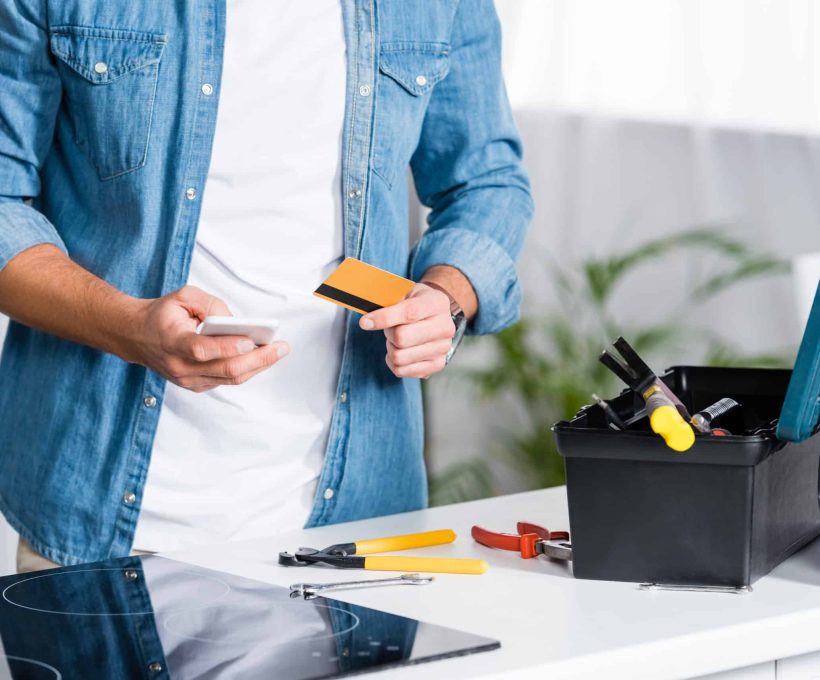 cropped view of man holding smartphone and credit card near tool box